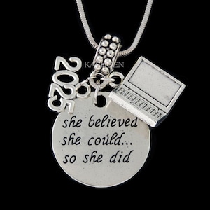 May include: Silver necklace with a charm that says "she believed she could... so she did" and a laptop charm. The necklace also has a charm with the year 2025.