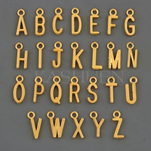 Puede incluir: Abalorios dorados con letras del alfabeto, cada uno con un peque&ntilde;o lazo en la parte superior para sujetarlos a joyas u otras manualidades. Las letras de la A a la Z se muestran en una cuadr&iacute;cula ordenada sobre un fondo gris. Los abalorios son todos en una fuente sans-serif.