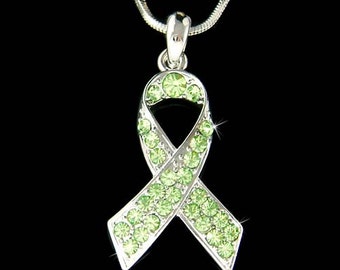 May include: A silver necklace with a green crystal ribbon charm. The ribbon is a symbol of awareness and support for various causes.