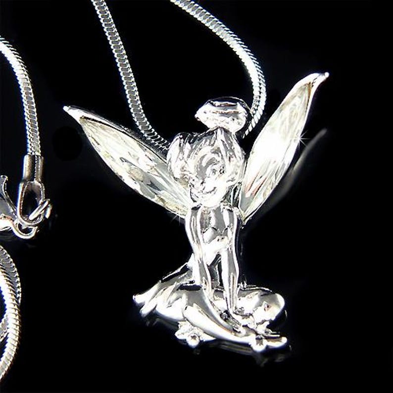 Puede incluir: Collar con colgante plateado que representa un hada. El hada est&aacute; representada con alas detalladas y est&aacute; sentada. La cadena del collar es una fina cadena de serpiente plateada. El fondo es negro.