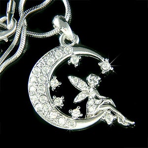Pode incluir: Um colar de prata com um pingente de lua crescente com uma fada de cristal sentada na lua. O pingente é incrustado com cristais transparentes.