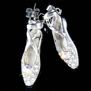Op de afbeelding: Een paar zilveren ballerina-oorbellen met heldere kristallen steentjes. De oorbellen zijn ontworpen met een delicaat, gekruist banddetail.