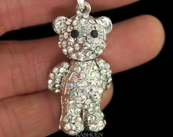 May include: A silver-toned pendant shaped like a teddy bear, fully encrusted with clear, sparkling rhinestones. The bear features two small, round black stones for eyes and a vest-like pattern on its torso with iridescent, multi-coloured crystals.