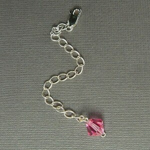 Peut inclure: Une chaîne en argent avec un charme en cristal rose. La chaîne mesure environ 5 cm de long et est munie d'un fermoir à ressort.
