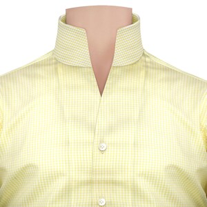 May include: A close-up of a yellow dress shirt with a distinctive collar. The shirt has a subtle checkered pattern and two white buttons. The collar is a contrasting white and yellow checkered pattern.