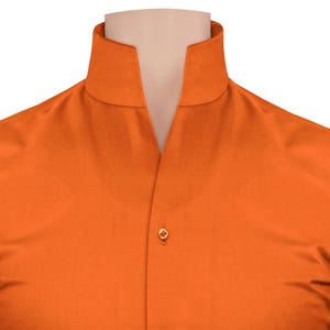 May include: Close-up of an orange shirt with a mandarin collar. The shirt is buttoned at the centre with a single, round, gold-coloured button. The fabric has a subtle texture, and the collar is open at the neck.