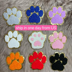 May include: Nine colorful paw print patches with gold glitter trim. The patches are in various colors, including gray, blue, purple, white, pink, orange, red, and black. The text "ship in one day from US" is visible.