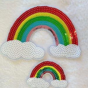 May include: Two rainbow-colored sequin patches with white cloud shapes. The larger rainbow has red, yellow, green, blue, and pink stripes. The smaller rainbow has red, yellow, green, blue, and purple stripes.