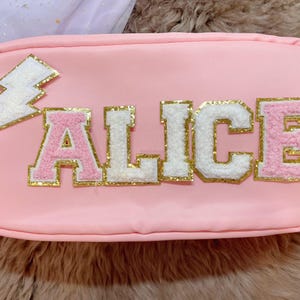 May include: Pink zippered pouch with a white lightning bolt and the name "ALICE" in pink, white, and gold letters.