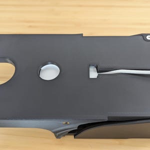 May include: A black plastic cable management box with a white cable running through it. The box has a circular opening and a slot for the cable.