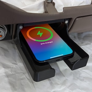 May include: A black smartphone with a charging animation on the screen is placed in a black wireless charging pad. The phone is 61% charged. The charging pad is in a car's center console.