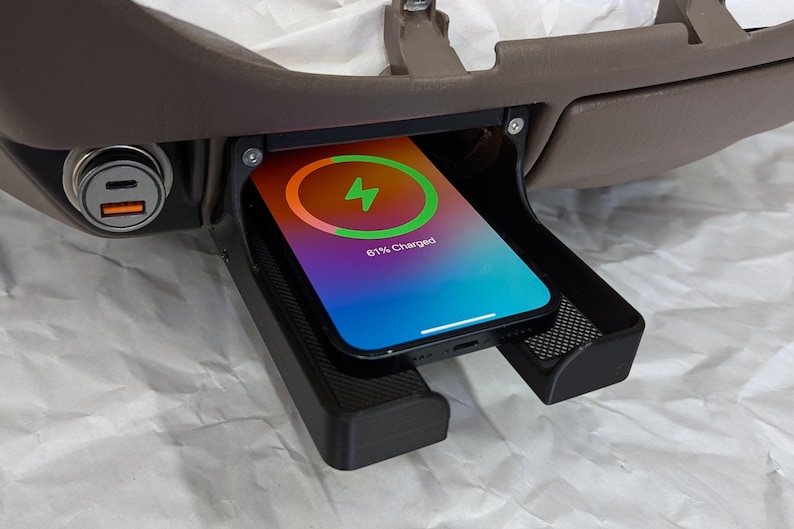 May include: A black smartphone with a charging animation on the screen is placed in a black wireless charging pad. The phone is 61% charged. The charging pad is in a car's center console.