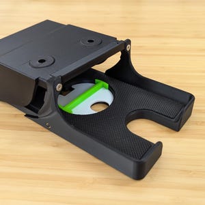 May include: A black plastic phone stand with a green accent. The stand is open and has a textured surface.
