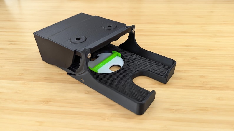 May include: A black plastic phone stand with a green accent. The stand is open and has a textured surface.