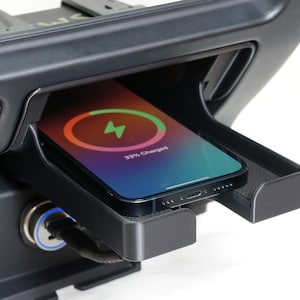 May include: A black car console with an integrated wireless charging pad. A smartphone rests on the pad, showing a charging symbol and the text "33% Charged". The console also has a 12V power outlet.