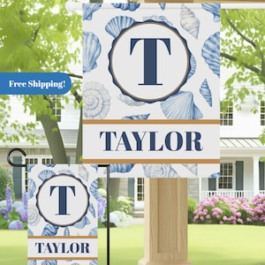 May include: A personalized garden flag featuring a seashell pattern in shades of blue and white. The flag includes a large initial "T" within a circular frame and the name "TAYLOR" in bold letters. The flag is displayed outdoors.