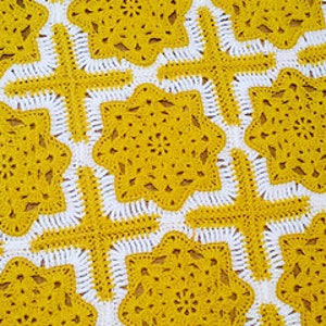 May include: A crocheted blanket with a geometric pattern in yellow and white. The blanket is made up of repeating squares with a starburst design in the center.