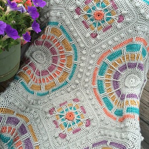 May include: A crocheted blanket with a geometric pattern in shades of gray, pink, orange, and teal.