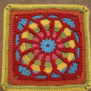 May include: A colourful crocheted square with a geometric pattern in shades of red, orange, yellow, green, blue, and pink.