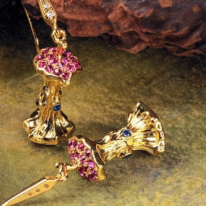 Könnte beinhalten: Ein Paar goldene Ohrringe mit einem Baumstamm-Design. Die Ohrringe sind mit rosa und blauen Edelsteinen verziert.