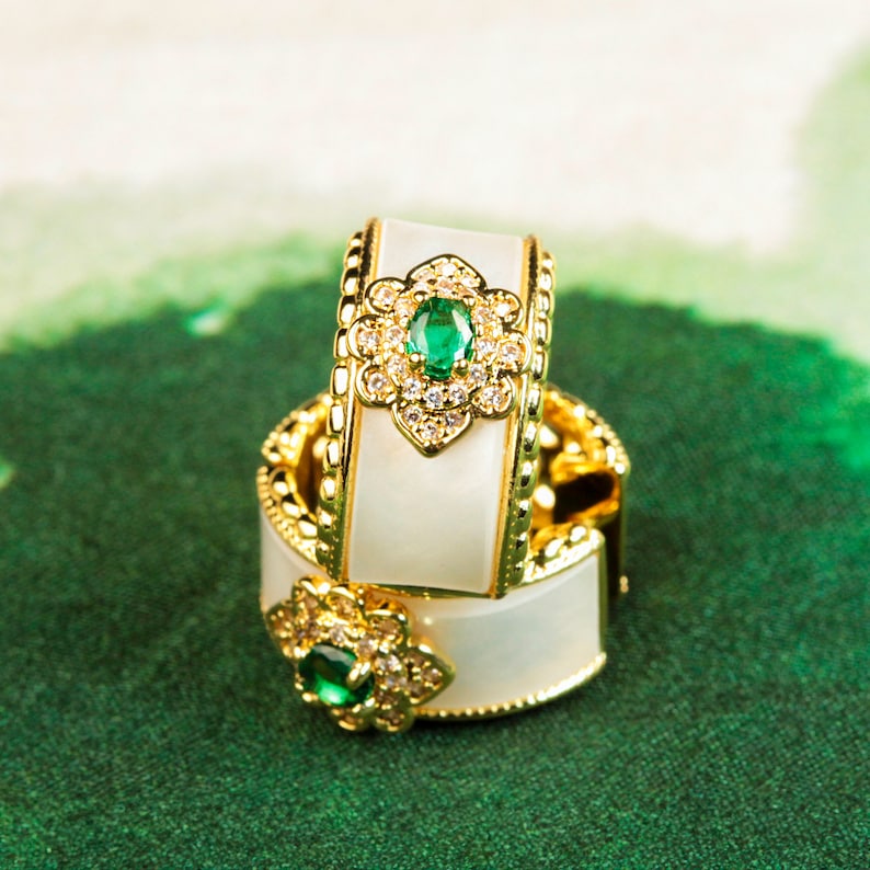 May include: Two white and gold hoop earrings with a green gemstone and clear rhinestones in a floral design.