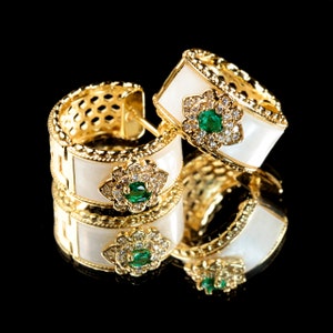 May include: A pair of gold hoop earrings with white enamel and green gemstones. The earrings are set with small diamonds and have a floral design.