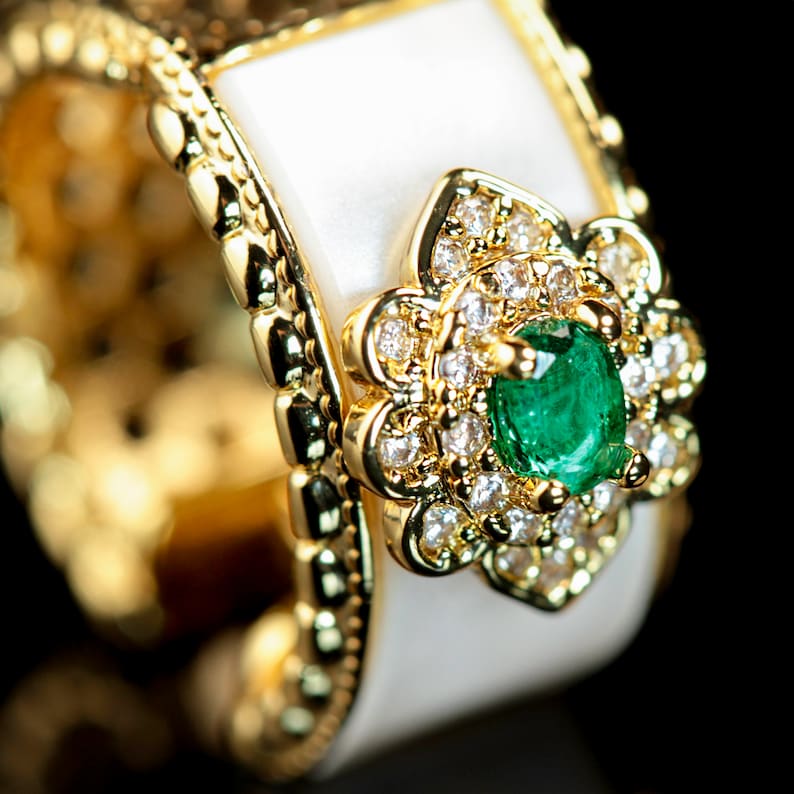 May include: A gold ring with a white enamel band and a green emerald gemstone surrounded by smaller diamonds in a flower design.