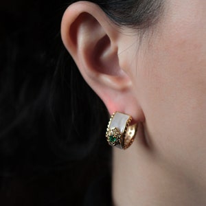 May include: Gold hoop earrings with a white oval-shaped stone and a green gemstone accent.