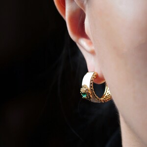 May include: White and gold hoop earrings with a green gemstone accent.