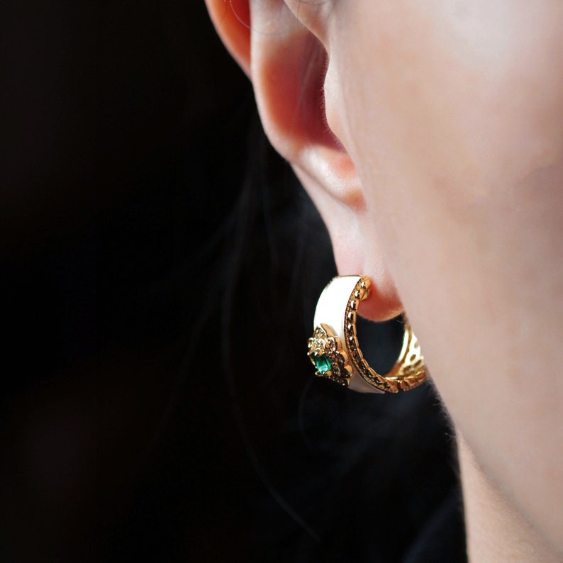 May include: White and gold hoop earrings with a green gemstone accent.