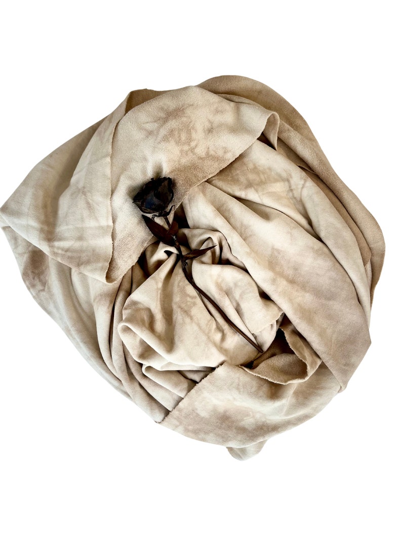 May include: A beige fabric scarf with a brown, dried rose tucked inside. The fabric has a tie-dye pattern.