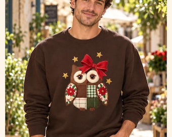 May include: A brown crewneck sweatshirt featuring a central applique of an owl with large eyes, a red bow on its head, and a patchwork body pattern of green, white, and red floral motifs. The design includes small yellow stars surrounding the owl.