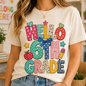 May include: A cream-coloured t-shirt featuring a colourful graphic with the text "HELLO 6TH GRADE" in a patchwork-style font. The design includes patterns like polka dots, gingham, and florals, accented with a blue bow, a red apple, and a yellow pencil.