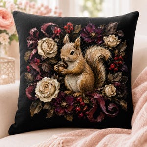 Könnte beinhalten: Ein quadratisches schwarzes Dekokissen mit einer zentralen Illustration eines braunen Eichhörnchens, das eine Eichel hält. Das Eichhörnchen ist von einem detaillierten Arrangement aus cremefarbenen Rosen, dunkelvioletten Blumen, roten Beeren und dunkelgrünen Blättern umgeben.