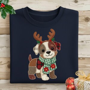 Può includere: Felpa blu navy con un cane patchwork con corna di renna e una sciarpa a quadri verdi. Il cane ha una combinazione di colori marrone, bianco e rosso, con accenti di agrifoglio. Abbigliamento festivo per le vacanze.