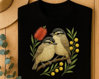 Puede incluir: Camiseta negra de manga larga con un diseño bordado de dos pájaros posados en una rama. Los pájaros tienen plumas marrones y blancas, con una flor roja y acentos florales amarillos. La camiseta está hecha de un material suave y cómodo.