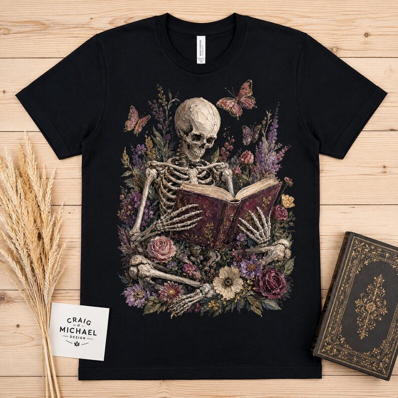 Skeleton reading book surrounded by flowers and butterflies on black t-shirt.