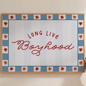 May include: A framed print with the words "LONG LIVE Boyhood" in red script. The background has vertical blue and white stripes. The frame is light wood with a blue border featuring red starburst designs.