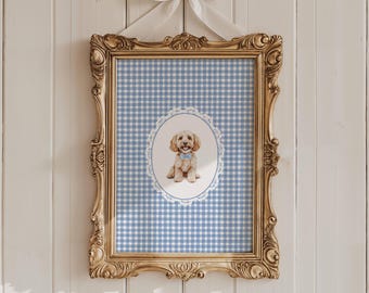 May include: A framed print with a watercolour illustration of a golden dog wearing a blue bow tie, set against a blue and white gingham background. The ornate gold frame is hung on a white wooden wall.