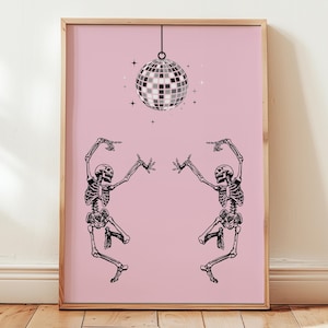 May include: A framed print featuring a pink background with a black and white illustration. The illustration depicts two dancing skeletons, a disco ball, and stars. The print is in a wooden frame.