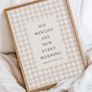 May include: A framed print with a light brown wooden frame. The artwork has a beige and white gingham pattern background. The text "HIS MERCIES ARE NEW EVERY MORNING" is displayed on a light beige rectangle. The text "LAMENTATIONS 3:23" is below the quote.