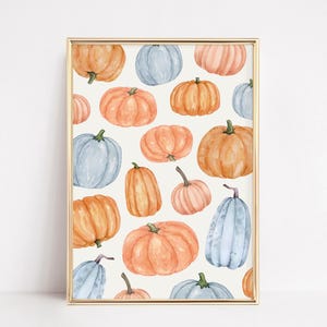 May include: A framed print featuring a watercolor pattern of pumpkins in shades of orange, peach, and blue against a cream background. The pumpkins vary in size and shape, with green stems. The frame is gold.