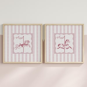 Puede incluir: Dos cuadros enmarcados con ilustraciones de caballos de carrusel. Las obras presentan caballos de carrusel rosas sobre un fondo a rayas rosas y blancas. Los marcos son de madera clara. El diseño general tiene una estética vintage, adecuada para una habitación infantil.