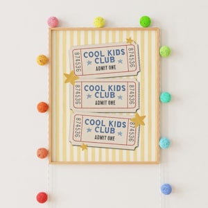 May include: A framed print featuring three horizontal ticket stubs with the text COOL KIDS CLUB and ADMIT ONE in blue, accented by yellow stars on a yellow and white vertical striped background, surrounded by colorful decorative yarn balls.