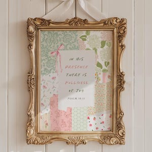 Puede incluir: Una obra de arte enmarcada con un marco dorado y ornamentado. La obra presenta un diseño de patchwork con telas florales y estampadas en colores pastel. El texto "IN HIS PRESENCE THERE IS FULLNESS OF JOY" se muestra sobre un fondo blanco. Se adjunta una cinta rosa.