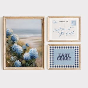 May include: Set of three framed art prints. The largest print features a coastal landscape with blue hydrangeas. The second print is a postcard design with the text "Meet me at the beach." The third print has the text "East Coast" on a blue gingham background.
