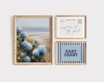 May include: Set of three framed art prints. The largest print features a coastal landscape with blue hydrangeas. The second print is a postcard design with the text "Meet me at the beach." The third print has the text "East Coast" on a blue gingham background.