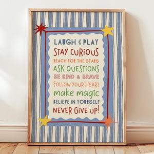May include: A framed wall art print featuring a light blue and white striped background with a central scalloped cream panel. The text reads: LAUGH & PLAY, STAY CURIOUS, REACH FOR THE STARS, ASK QUESTIONS, BE KIND & BRAVE, FOLLOW YOUR HEART, make magic, BELIEVE IN YOURSELF, NEVER GIVE UP! Red and yellow star accents decorate the corners.