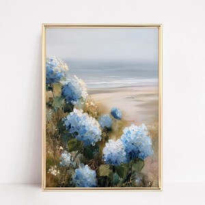 May include: A framed painting featuring a coastal landscape with blue hydrangea flowers in the foreground. The artwork has a gold frame and depicts a beach scene with a soft, muted color palette, evoking a sense of tranquility.