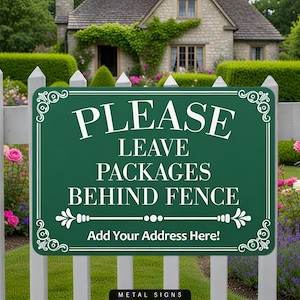 May include: A dark green metal sign with white text that reads "PLEASE LEAVE PACKAGES BEHIND FENCE". The sign is framed with white decorative flourishes and is mounted on a white picket fence. The sign also has the text "Add Your Address Here!"